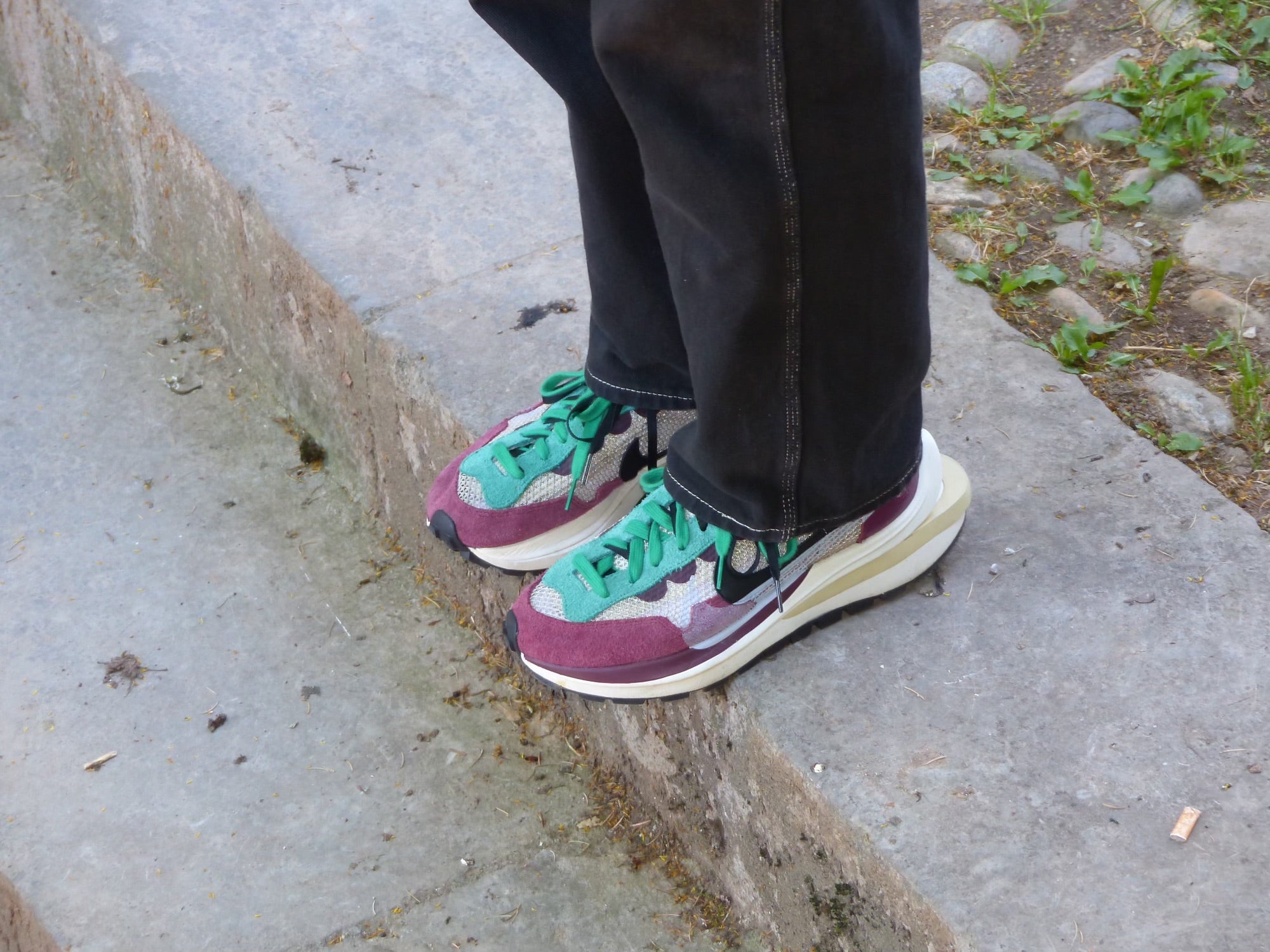 Paire de nike en collaboration avec sacaï violette et verte, sur un trottoir
